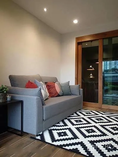 Townhouse for rent in Watthana, Bangkok - Cozy sitting room with gray sofa and patterned rug beside sliding wooden door.