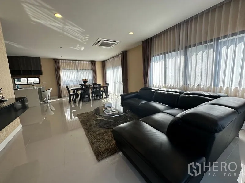 บ้าน ให้เช่าหรือขายในLam Luk Ka, Pathum Thani - พื้นที่รับแขกและรับประทานอาหารแบบเปิด พร้อมโซฟาหนังสีดำ ชุดโต๊ะกินข้าว และหน้าต่างรอบด้าน