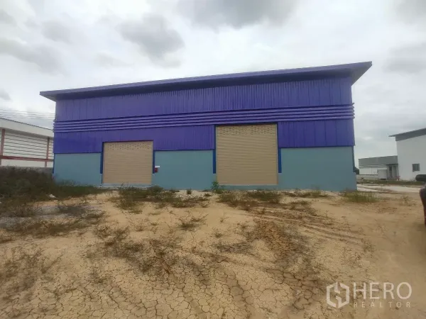 工厂 出售在Khlong Toei, Bangkok - 蓝色厂房外观，双卷闸大门与前方砂砾空地。