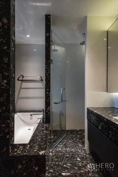 公寓 出租在Khlong Toei, Bangkok - 卫浴内设玻璃淋浴间、浴缸与深色大理石饰面。