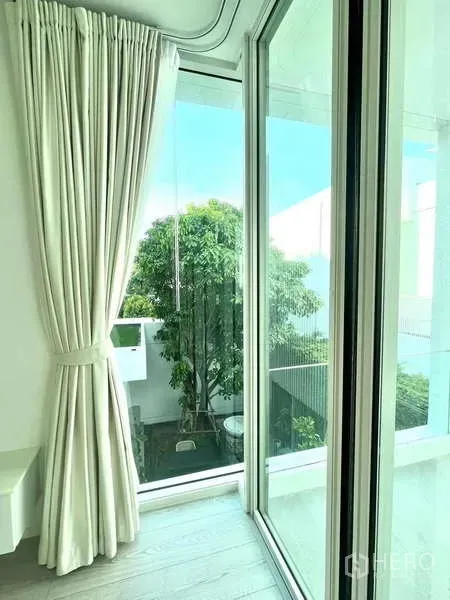 独立式住宅 出租或出售在Bang Phli, Samut Prakan - 落地窗配轻薄窗帘，可眺望绿色庭院景观。