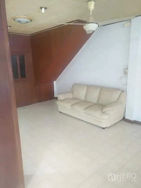 ทาวน์เฮาส์ ให้เช่า - ห้องนั่งเล่นสว่าง พื้นกระเบื้อง โซฟาสีครีม และผนังไม้ใต้บันได