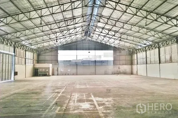 Warehouse for rent in Saphan Sung, Bangkok - Vast clear-span warehouse interior with high steel truss roof, skylights, and wide loading doors.