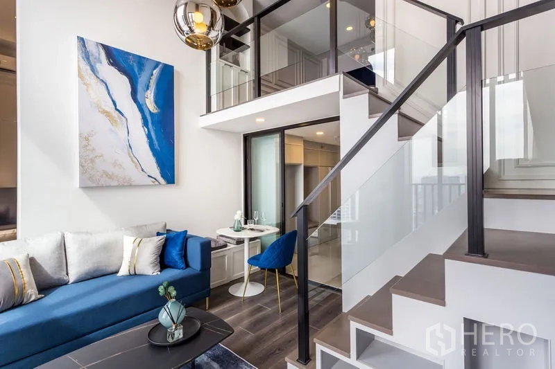 公寓 出租或出售在Chatuchak, Bangkok - 夹层楼梯与玻璃栏杆，上方俯看装饰画与用餐角的客厅