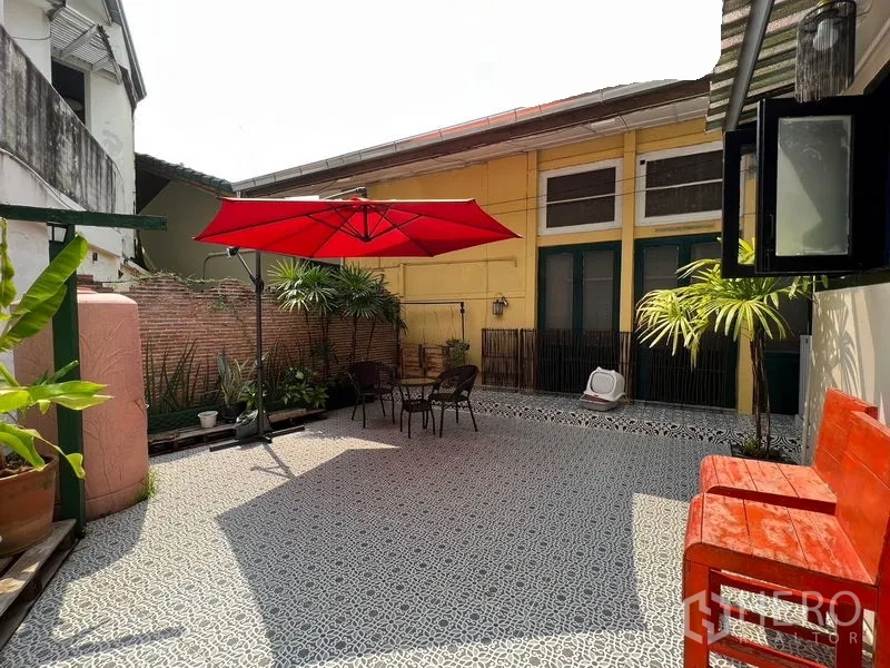 Townhouse for rent in Ratchathewi, Bangkok - Sunlit tiled courtyard with a red umbrella, bistro table set and tropical potted plants.