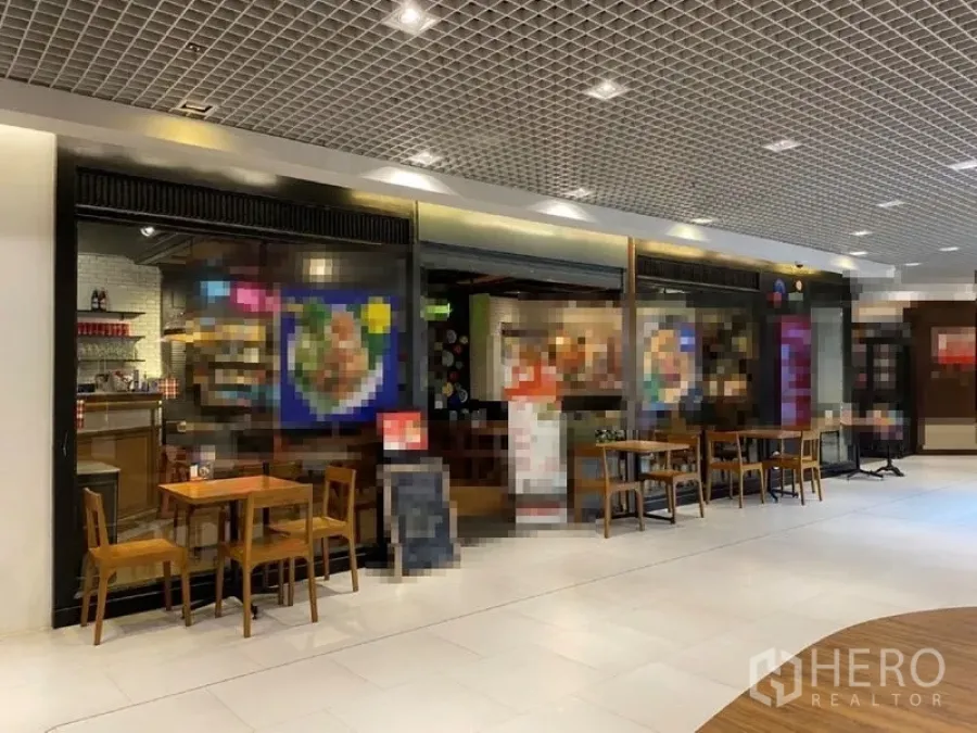 零售空间 出租在Khlong Toei, Bangkok - 商场走道旁的玻璃门面商铺，暖色灯光与咖啡式座位区。