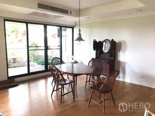 Condominium for rent in Sathon, Bangkok - Dining area with wooden table and chairs under a pendant light beside floor-to-ceiling windows and terrace.