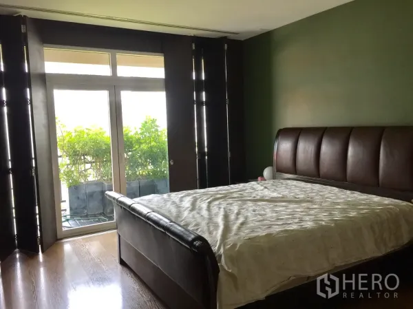 Condominium for rent in Watthana, Bangkok - Primary bedroom with dark wood bed, floor‑to‑ceiling doors and a leafy balcony outside.