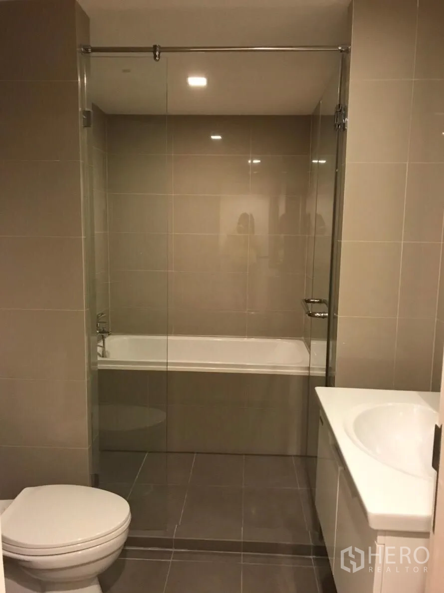 Condominium for rent in Watthana, Bangkok - Contemporary bathroom with glass-enclosed tub and shower, toilet and vanity.