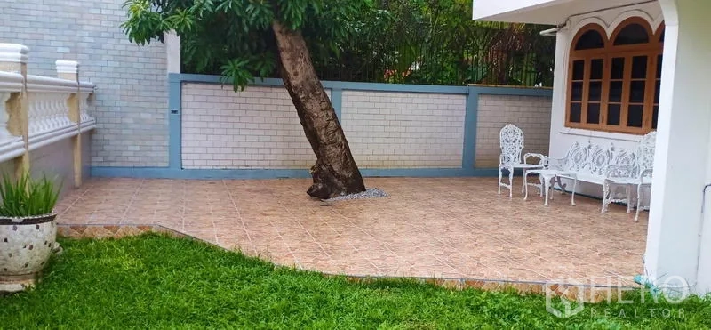 独立式住宅 出租在Watthana, Bangkok - 铺砖露台带树与白色户外桌椅，旁接草坪。