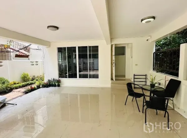 บ้าน ให้เช่า - ระเบียงนั่งเล่นแบบร่มรื่น มีชุดโต๊ะเก้าอี้และประตูกระจกสไลด์เชื่อมสวน.