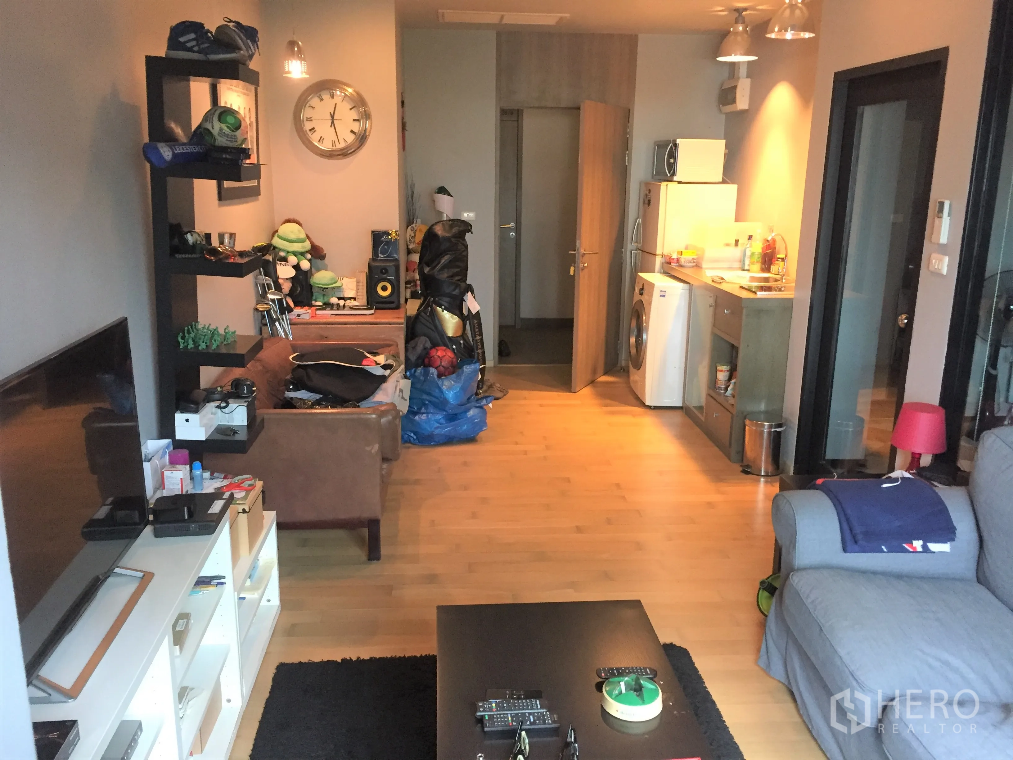 คอนโด ให้เช่าหรือขายในWatthana, Bangkok - ห้องนั่งเล่นแบบโอเพ่นพร้อมพื้นไม้ ชั้นวางทีวี และครัวขนาดกะทัดรัดพร้อมเครื่องซักผ้า