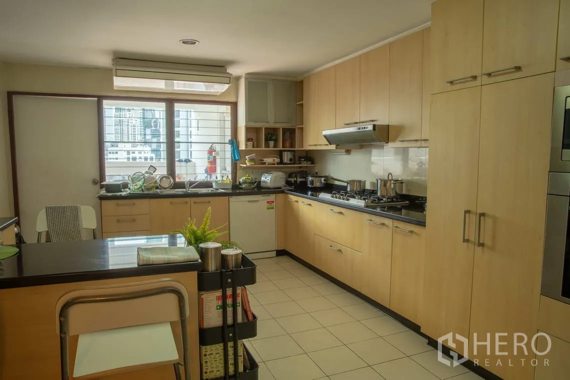 Apartment for rent in Khlong Toei, Bangkok - Light wood kitchen with gas stove, island counter, and city-view window.