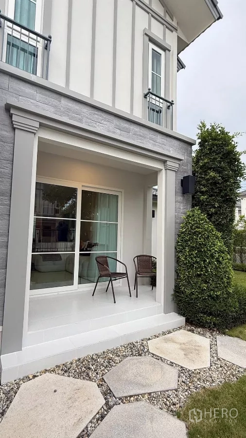 บ้าน ให้เช่าในBang Phli, Samut Prakan - ชานหน้าบ้านพร้อมเก้าอี้สองตัวและทางเดินแผ่นหินข้างพรรณไม้จัดสวน.