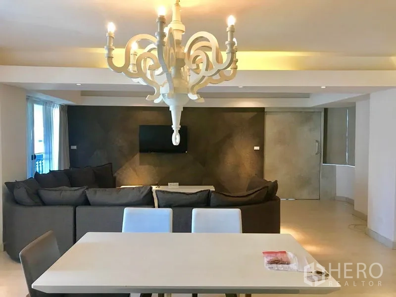 Condominium for rent or sale in Watthana, Bangkok - Dining table and chandelier facing a textured accent wall with mounted TV in the living area.
