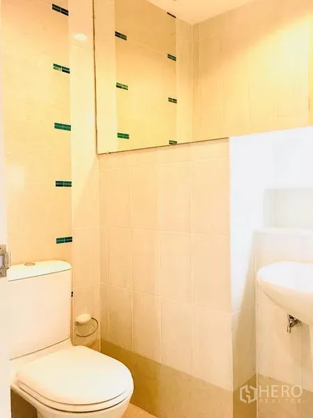 Townhouse for rent in Prawet, Bangkok - Compact bathroom with toilet, sink, large mirror, and light beige tiles.