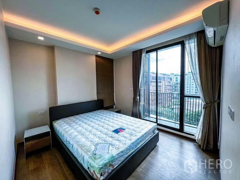 Condominium for sale in Huai Khwang, Bangkok - Master bedroom with recessed lighting and floor-to-ceiling sliding doors opening to a balcony with city views.
