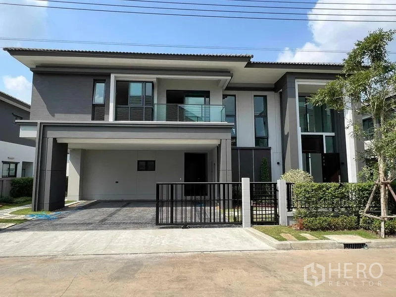 Detached House for rent in Khlong Sam Wa, Bangkok - Front elevation of the two-storey house with balcony, wide carport and secure front gate.