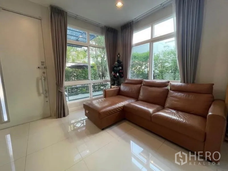 บ้าน ให้เช่าในLat Krabang, Bangkok - มุมนั่งเล่นพร้อมโซฟาหนังรูปตัวแอล หน้าต่างสูง และวิวสวน