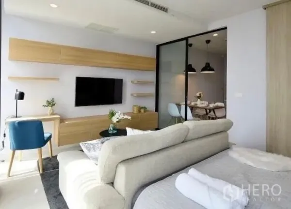 คอนโด ให้เช่าในPathum Wan, Bangkok - โซนนั่งเล่นมีทีวีติดผนัง ตู้ไม้โทนอ่อน และประตูกระจกบานเลื่อนสู่ห้องทานอาหาร