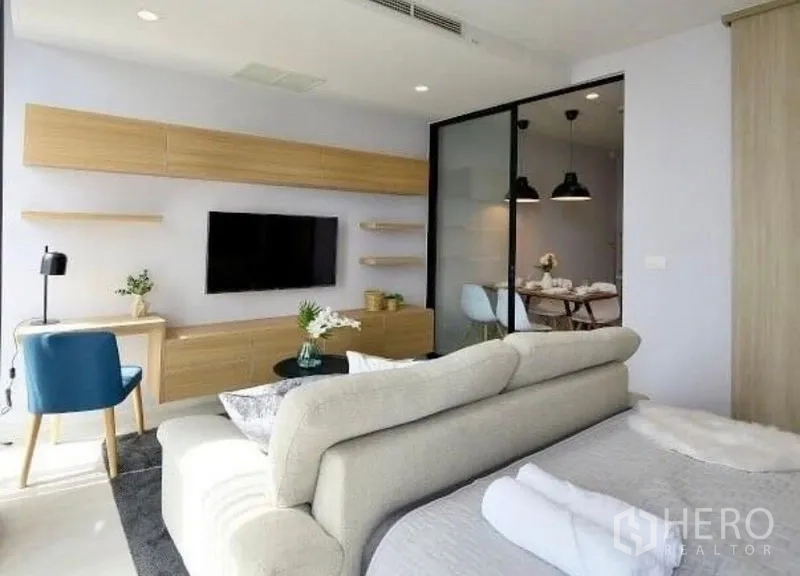 คอนโด ให้เช่าในPathum Wan, Bangkok - โซนนั่งเล่นมีทีวีติดผนัง ตู้ไม้โทนอ่อน และประตูกระจกบานเลื่อนสู่ห้องทานอาหาร