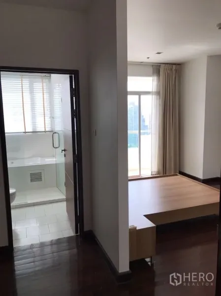 Condominium for rent in Watthana, Bangkok - Hallway of the condo showing a bright bedroom platform area and a bathroom with glass door and city light from a balcony window.