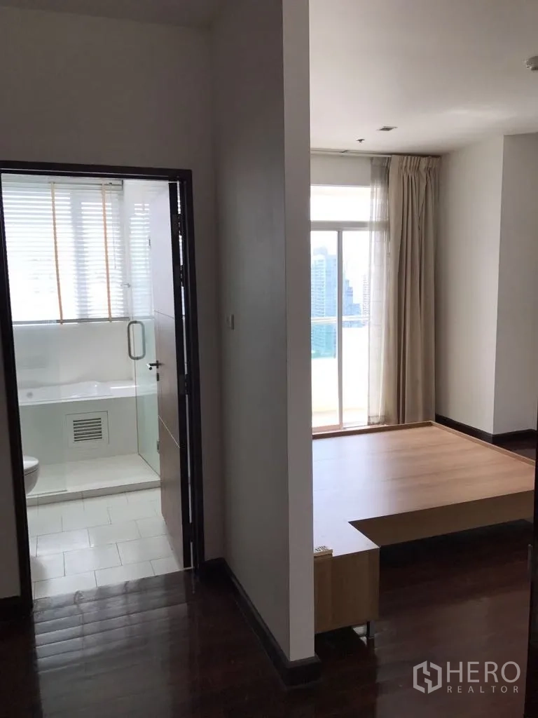 Condominium for rent in Watthana, Bangkok - Hallway of the condo showing a bright bedroom platform area and a bathroom with glass door and city light from a balcony window.