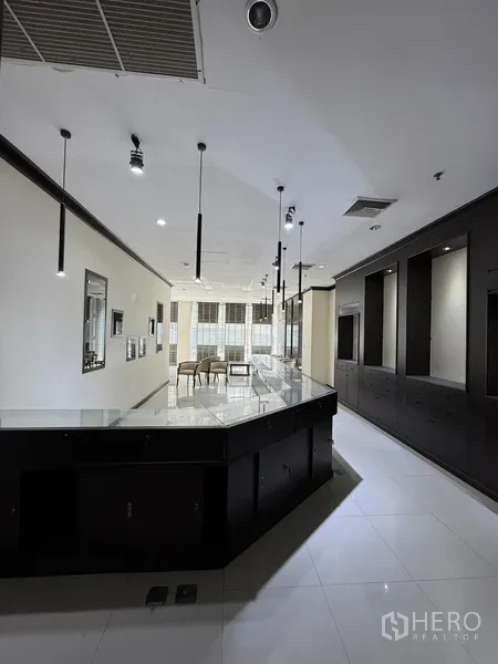 零售空间 出租在Sathon, Bangkok - 明亮的展厅内部，长服务台、吊灯与白色瓷砖地面。