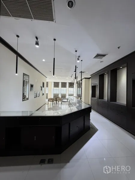 零售空间 出租在Sathon, Bangkok - 明亮的展厅内部，长服务台、吊灯与白色瓷砖地面。