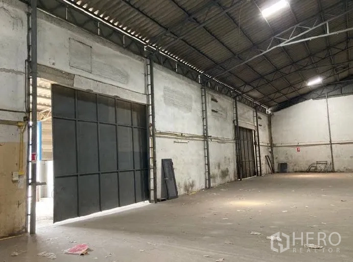 Factory for rent in Samut Prakan - Industrial hall showing large sliding steel doors, bright ceiling lights and a wide clear-span floor.