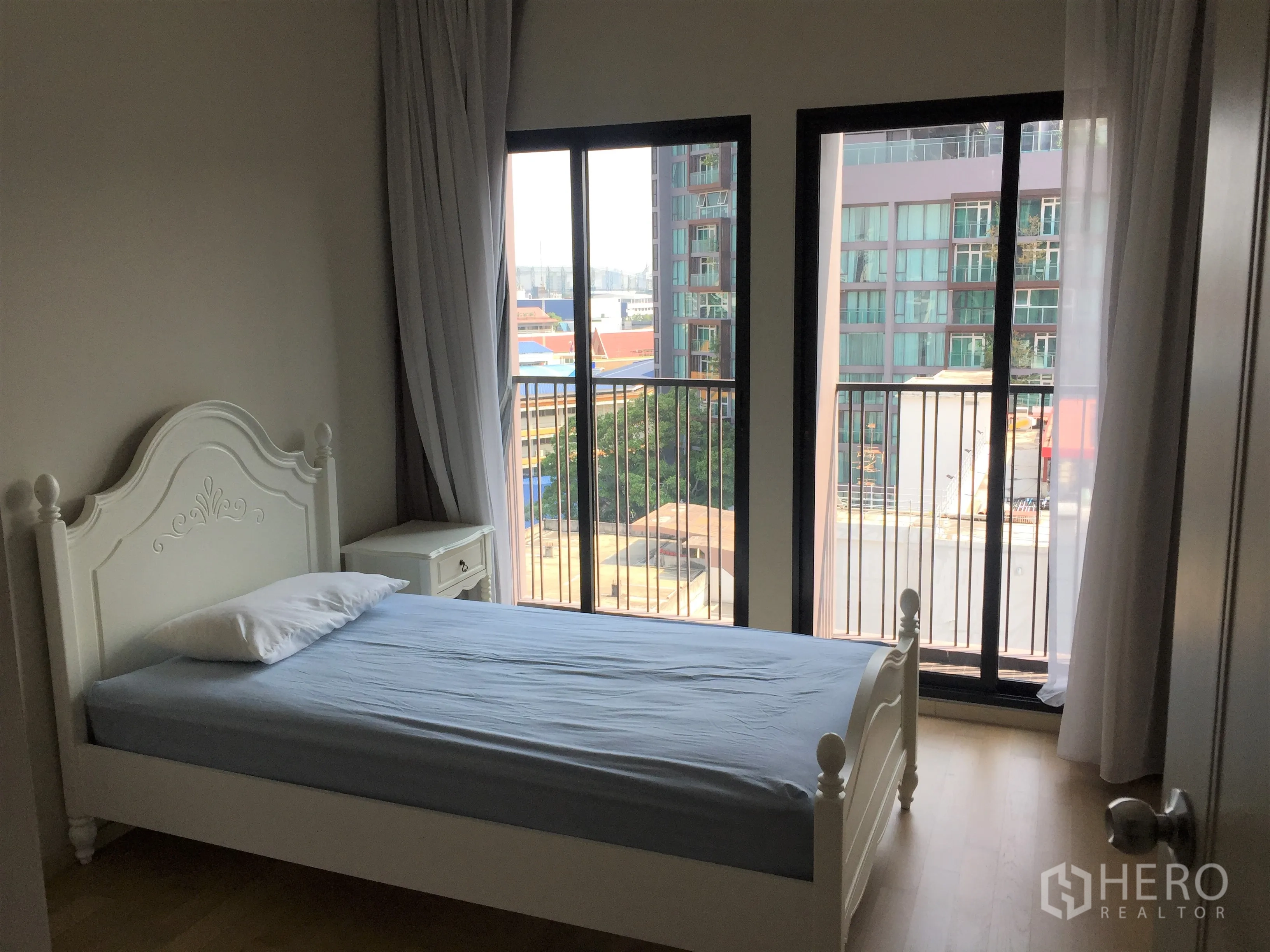 Condominium for rent or sale in Watthana, Bangkok - Cozy bedroom with white bedframe and sliding glass doors opening to a balcony with city views.