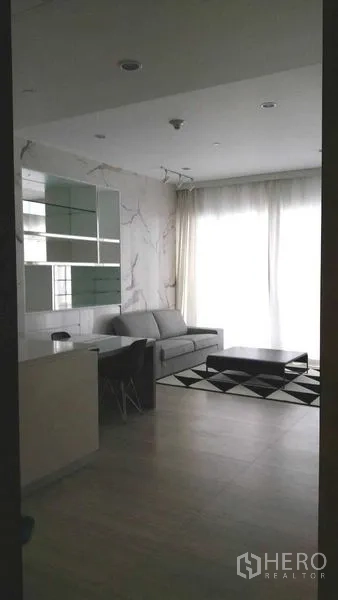 Condominium for rent in Pathum Wan, Bangkok - Bright lounge with full-height curtains, gray sofa, and low coffee table on a monochrome rug.