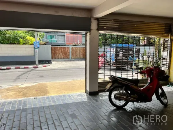 Townhouse for rent in Khlong Toei, Bangkok - Covered ground-floor parking with roller shutter opening to a quiet street.