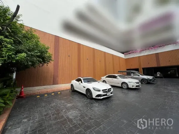 零售空间 出租在Watthana, Bangkok - 建筑前方的露天停车区，木质立面与多辆车辆可见。