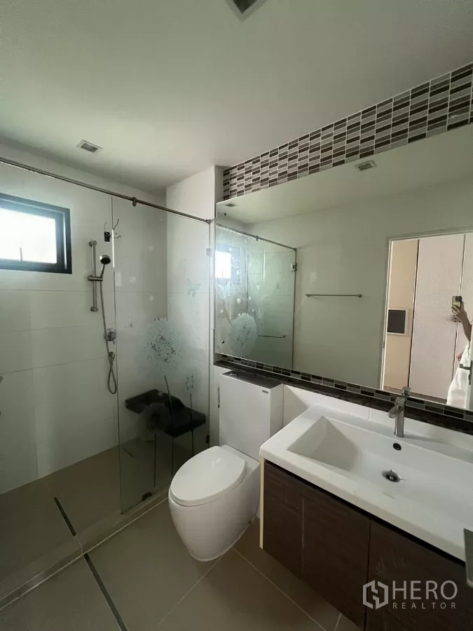 Detached House for sale in Bang Kapi, Bangkok - Contemporary bathroom with glass shower enclosure, long mirror, and vanity.