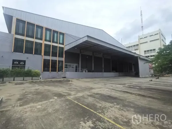 工厂 出租在Khlong Toei, Bangkok - 工厂外观，三层玻璃办公室与带顶装卸月台，前方大型车辆回转场地。