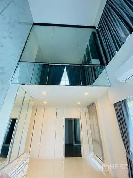 Detached House for sale in Bang Phli, Samut Prakan - Double-height room with mezzanine glass balustrade, mirrors and tall drapes.