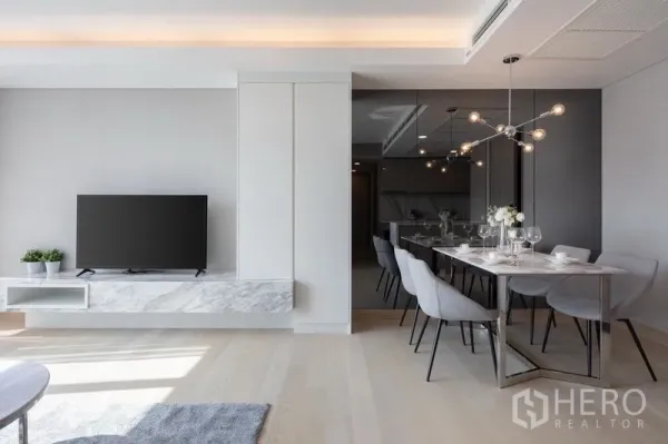 Condominium for rent in Khlong Toei, Bangkok - Modern dining space with designer light fixture beside a wall-mounted TV on a marble console and mirrored feature wall.