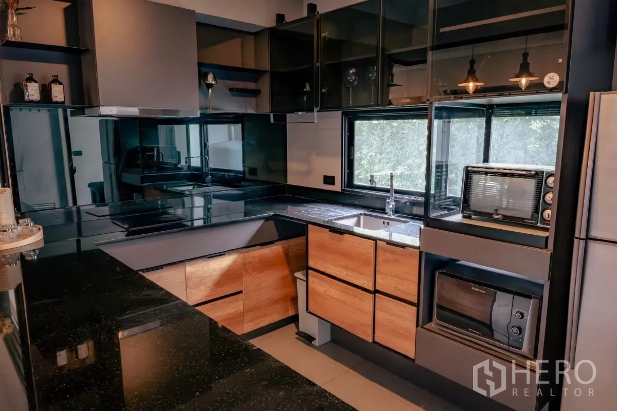 独立式住宅 出租或出售在Bang Phli, Samut Prakan - L形现代厨房，黑色石材台面、木质柜体与玻璃吊柜。