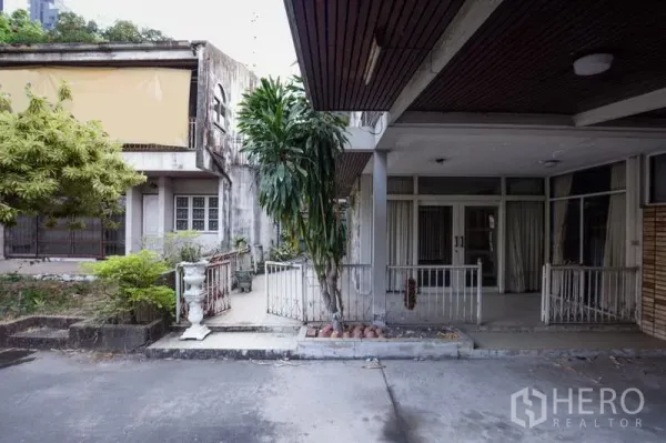 Detached House for rent in Khlong Toei, Bangkok - Front courtyard of the detached house with a covered carport, mature trees, and glass entry doors near BTS Thonglor.