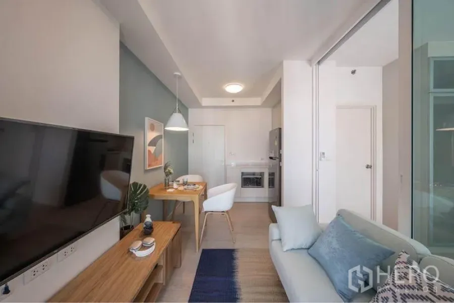 Condominium for sale in Huai Khwang, Bangkok - Living room view toward the entry and compact kitchenette beside a glass-partitioned bedroom.
