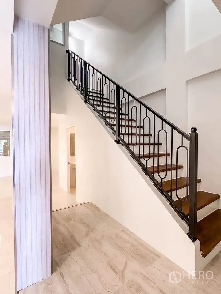 联排别墅 for sale in Wang Thonglang, Bangkok - 黑色金属栏杆楼梯与木踏板的挑高空间。
