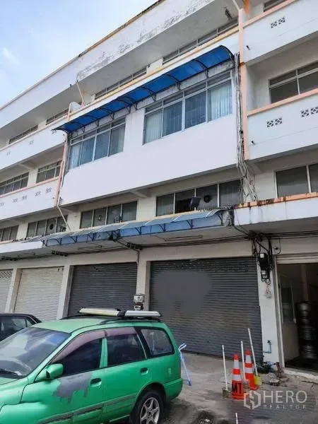 店屋 出售在Pathum Thani - 街向店屋外观，卷闸门关闭并有停车位。