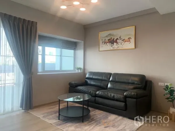 联排别墅 出租 - 客厅配黑色皮沙发、大窗与窗帘及圆形玻璃茶几。