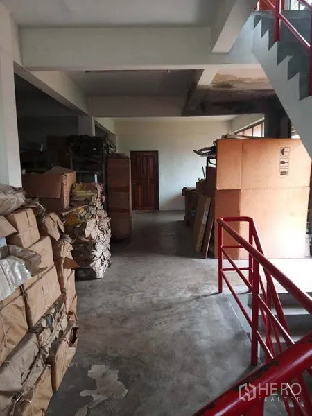 零售空间 出售在Bang Khun Thian, Bangkok - 储物楼层，红色楼梯扶手，走道两侧堆放纸箱。