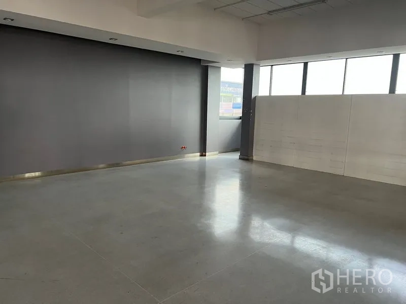 Office Space for rent in Mueang Samut Prakan, Samut Prakan - Bright empty workspace with large windows and a dark feature wall.