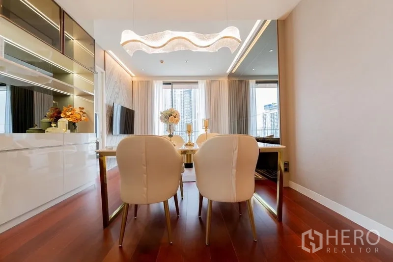 公寓 出租在Watthana, Bangkok - 明亮餐区，波浪形吊灯、金色餐桌与白色椅子，落地窗俯瞰城市景观。
