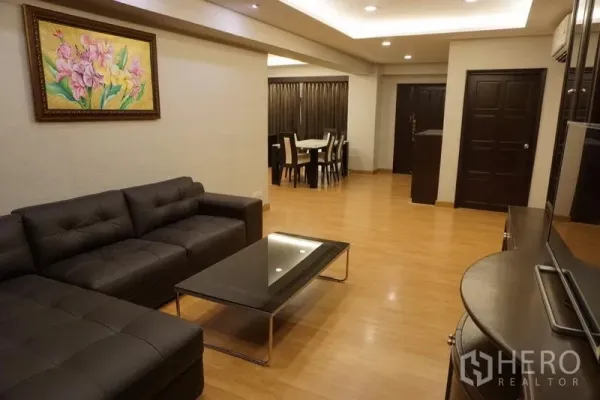 Condominium for rent in Watthana, Bangkok - Spacious living and dining area with L‑shaped sofa, wood floors and recessed ceiling lights.