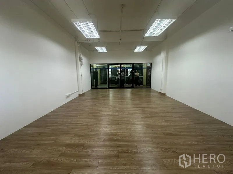 สำนักงาน ให้เช่าในChatuchak, Bangkok - ห้องสำนักงานทรงยาวหันสู่ผนังกระจก พื้นลายไม้ และแผงไฟเพดานหลายจุด