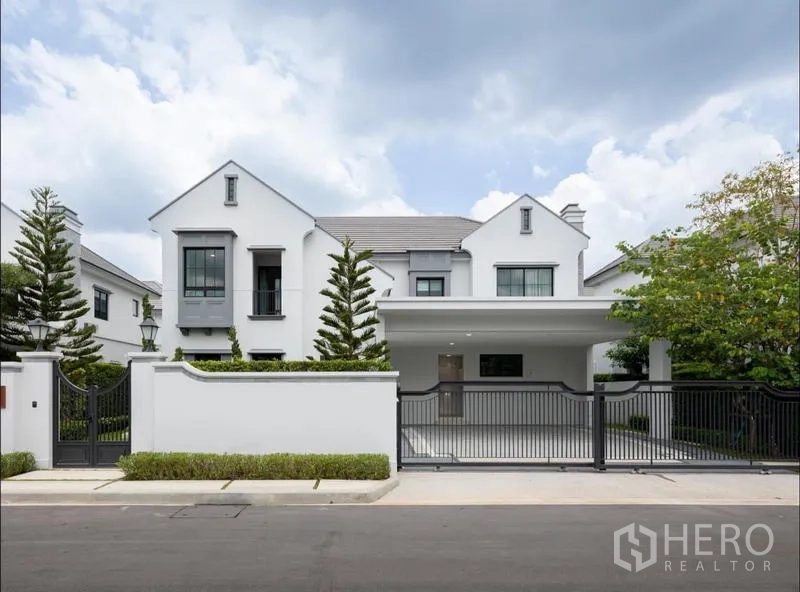 Detached House for sale in Saphan Sung, Bangkok - Front elevation of gated two-storey house with carport and landscaped trees.